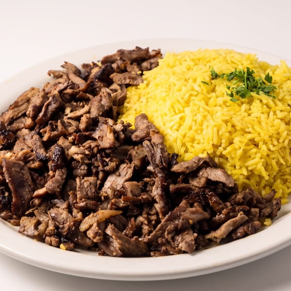 A white plate holds a generous serving of yellow rice with parsley and sliced brown meat.