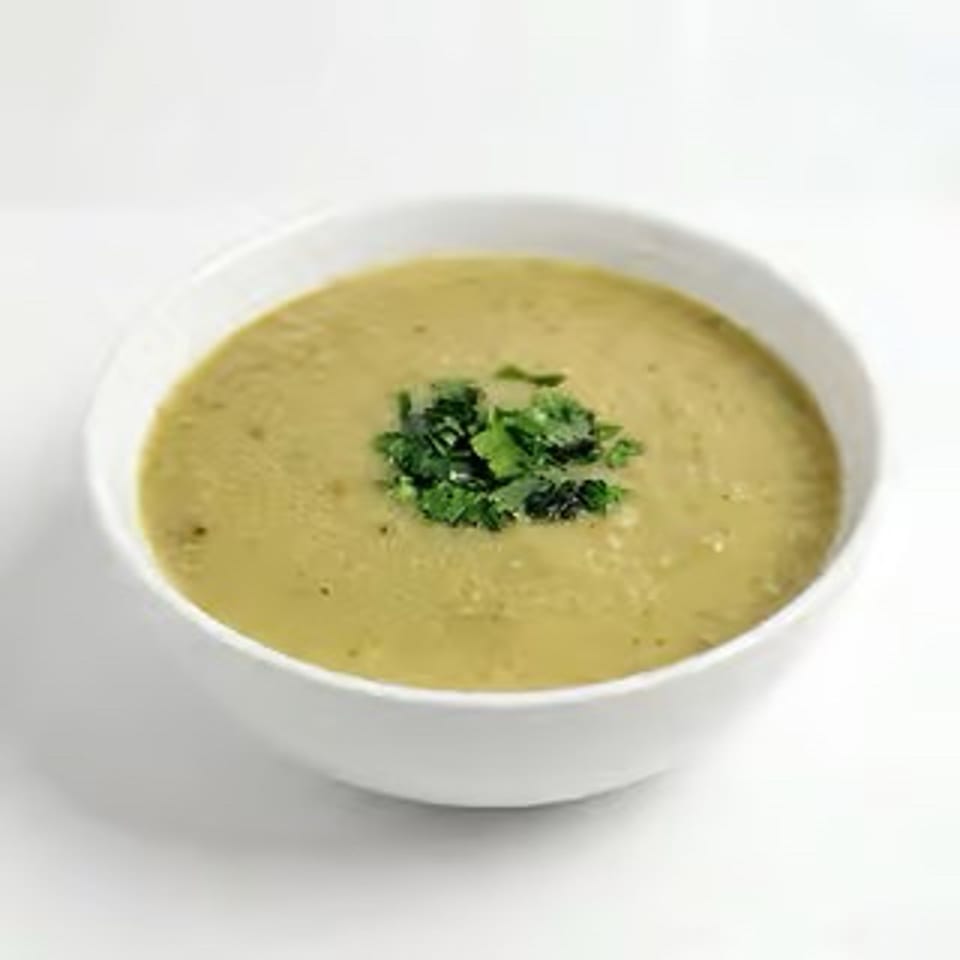 Bowl of creamy pale-yellow soup garnished with fresh chopped herbs.