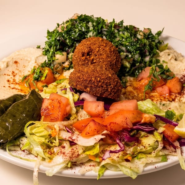Falafel platter with hummus, baba ghanoush, tabbouleh, salad, stuffed grape leaves, and a lemon wedge.