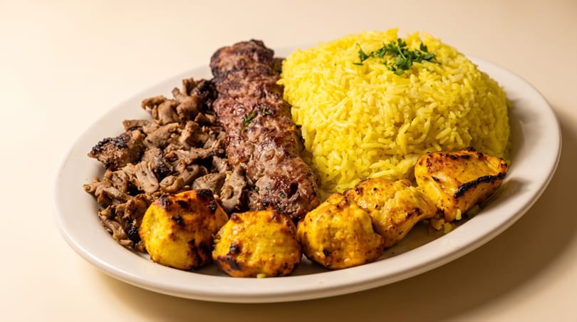 Plate with yellow rice, a long kebab, chopped meat, and grilled chicken pieces.