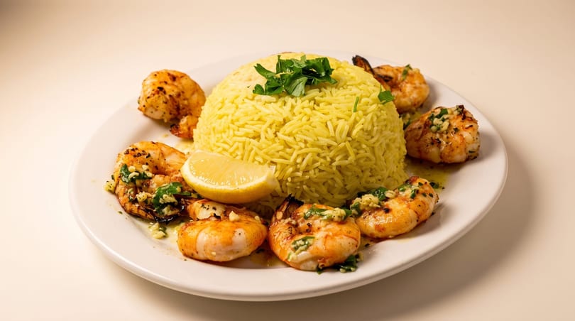 Grilled shrimp and yellow rice with lemon and parsley on a white plate.