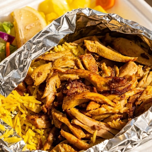 Takeout container with chicken and yellow rice in foil, side salad, and lemon wedges.