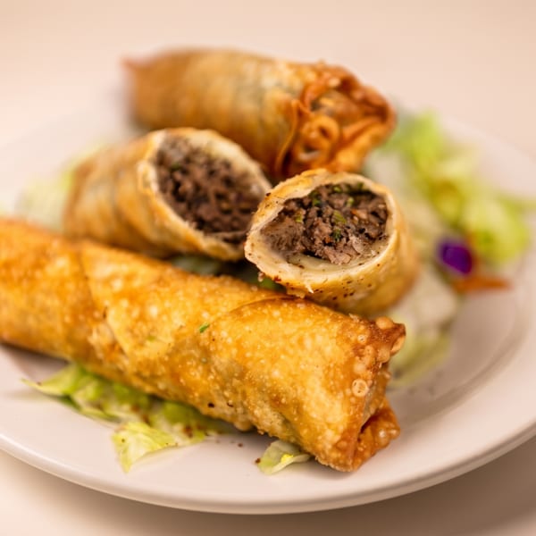 Three golden egg rolls, two cut open to show a savory meat filling, served on lettuce.