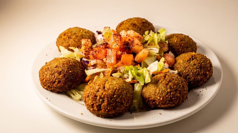 Plate of crispy falafel balls surrounding a fresh salad with diced tomatoes and lettuce.
